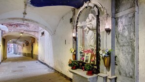 Ein enger Korridor mit einer Statue einer Frau, die ein Kind hält, einer Marmorbank und Blumentöpfen.