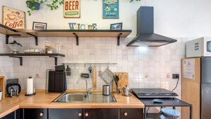 Eine moderne Küche mit Holzarbeitsplatte, Edelstahlspüle und schwarzen Schränken. Auf der Arbeitsfläche hängen Küchenutensilien, ein Kaffeeautomat und ein Toaster.