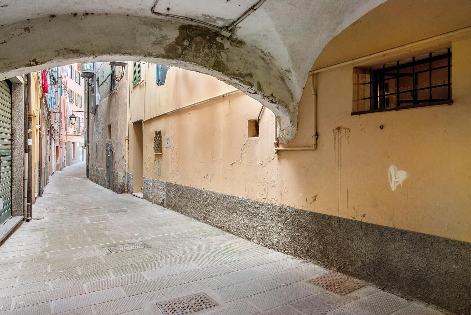 A narrow alleyway with a tiled floor, a low ceiling, and buildings on either side.