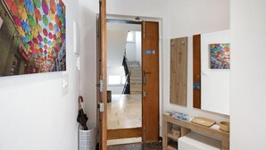 Un corridoio con una porta in legno che dà su una scala, una parete bianca decorata con un murale di ombrelli colorati e una mensola in legno con libri e una ciotola.