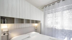 Una camera d'albergo con un letto, lampade sui comodini, una libreria e una finestra con tende leggere.