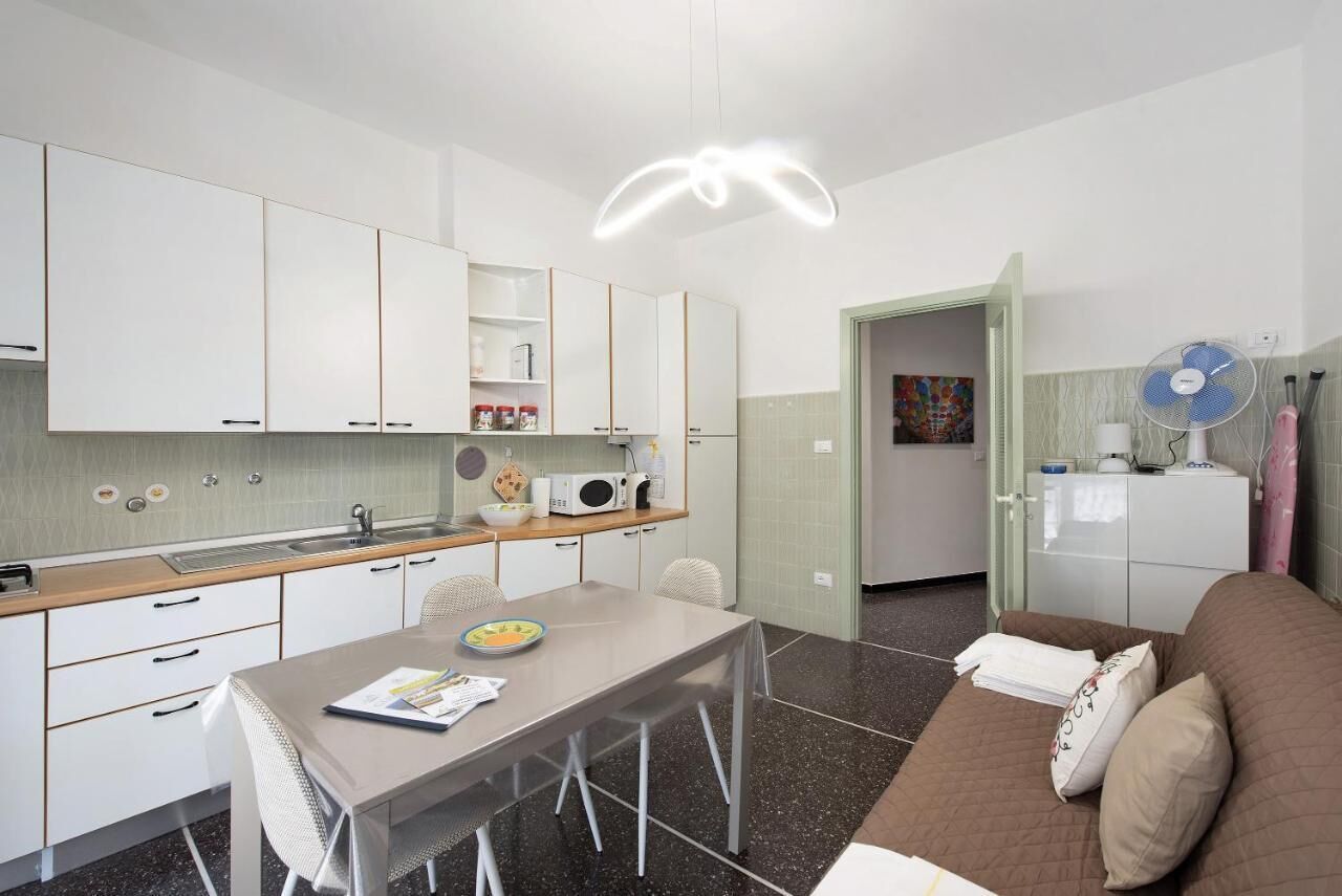 Een compacte keuken met witte kastjes, een eettafel en een bank in een woongedeelte.