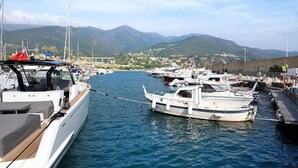 Una marina con imbarcazioni ormeggiate, un ponte sullo sfondo e un paesaggio montuoso.
