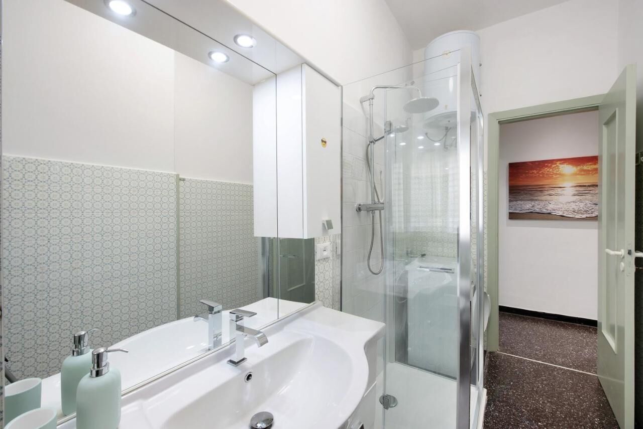 Une salle de bain moderne avec un grand miroir, un lavabo blanc et une douche à parois de verre.