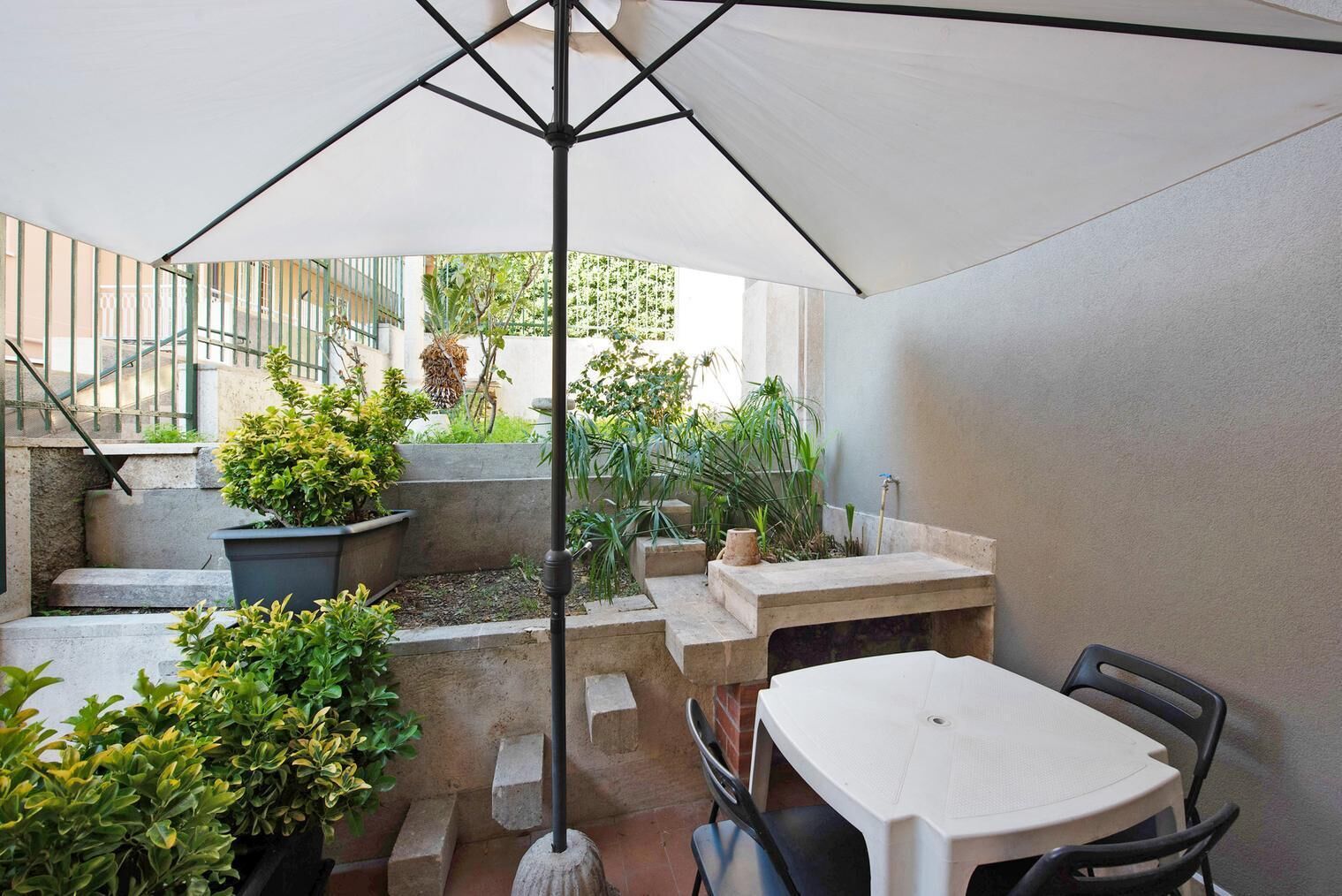 Un espace extérieur aménagé en terrasse, avec une table et des chaises, entouré de plantes en pot et d’un escalier.