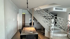 Moderni sisustus, jossa on ruokailutila, geometrisesti kuvioitu portaikko ja taustalla keittiö.