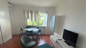 Uma sala de estar com televisão, mesa de jantar com cadeiras e uma janela com cortinas.