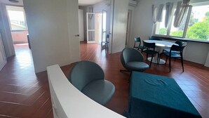 Uma área de refeições com mesa e cadeiras, um sofá e vista para o verde pela janela.