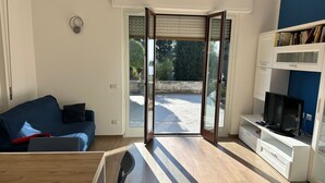 A modern living room with a blue sofa, a wooden dining table, and a TV on a white cabinet. - Casa Mimose - Two Bedroom Apartment, Sleeps 5 (Cogoleto)
