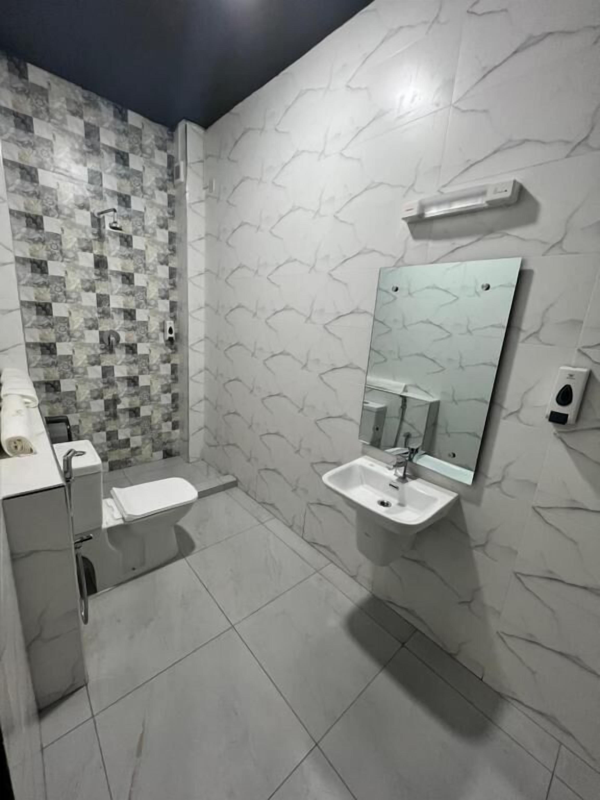 A modern bathroom with a tiled floor, a toilet, a sink with a mirror, and a shower area with a patterned tile wall.