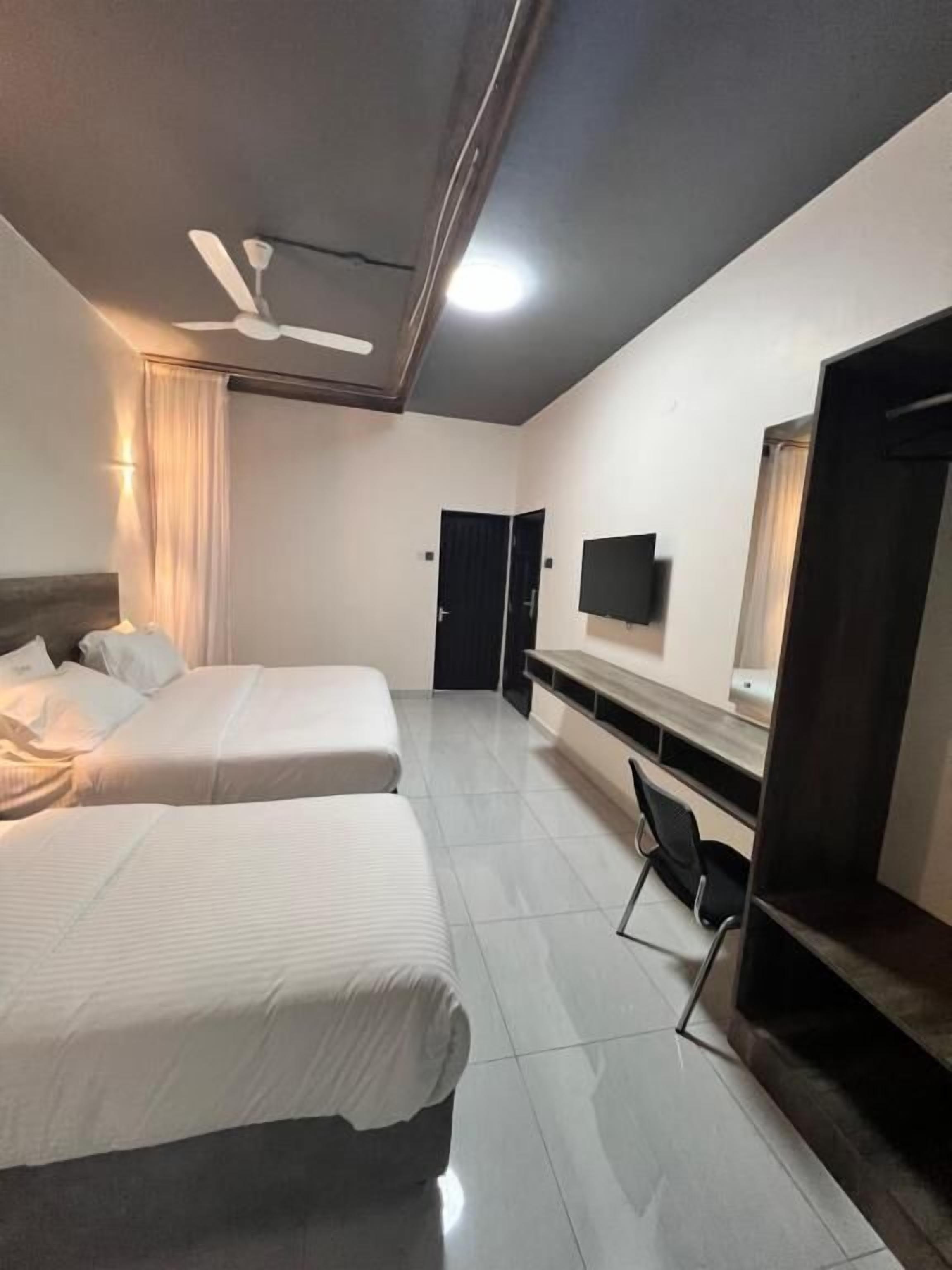 A hotel room with two beds, a ceiling fan, a TV, and a desk with a chair.