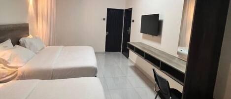 A hotel room with two beds, a ceiling fan, a TV, and a desk with a chair.