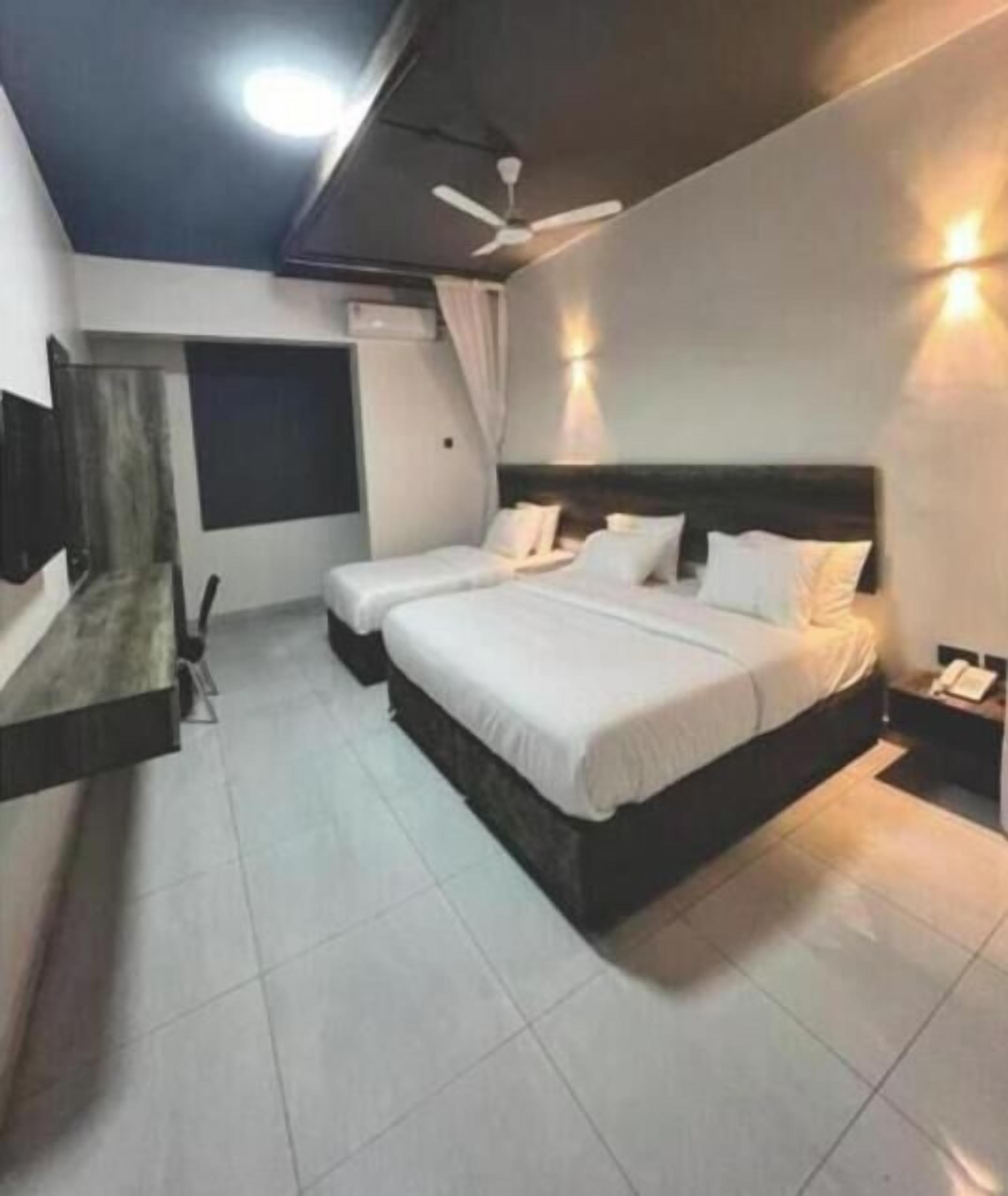 A modern hotel room with two beds, a flat-screen TV mounted on the wall, a ceiling fan, and a large window with curtains.