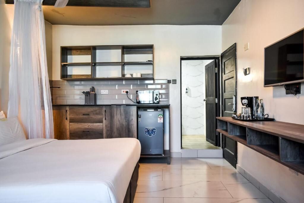 Une chambre d’hôtel compacte comprenant un lit, une kitchenette équipée d’un four à micro-ondes, d’un petit réfrigérateur et d’un téléviseur fixé au mur.