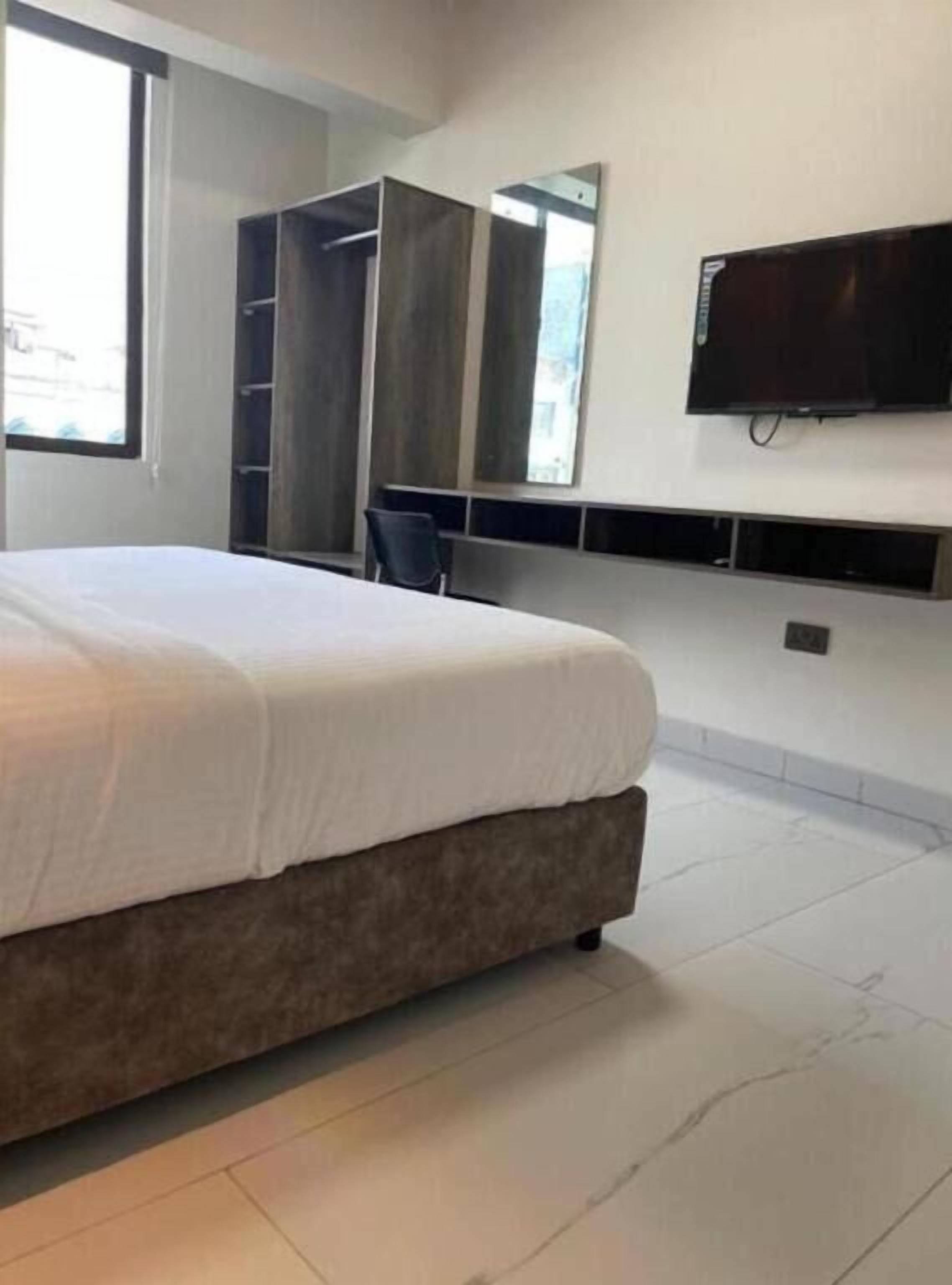A modern hotel room with a large bed, a wardrobe, a television, and a window.