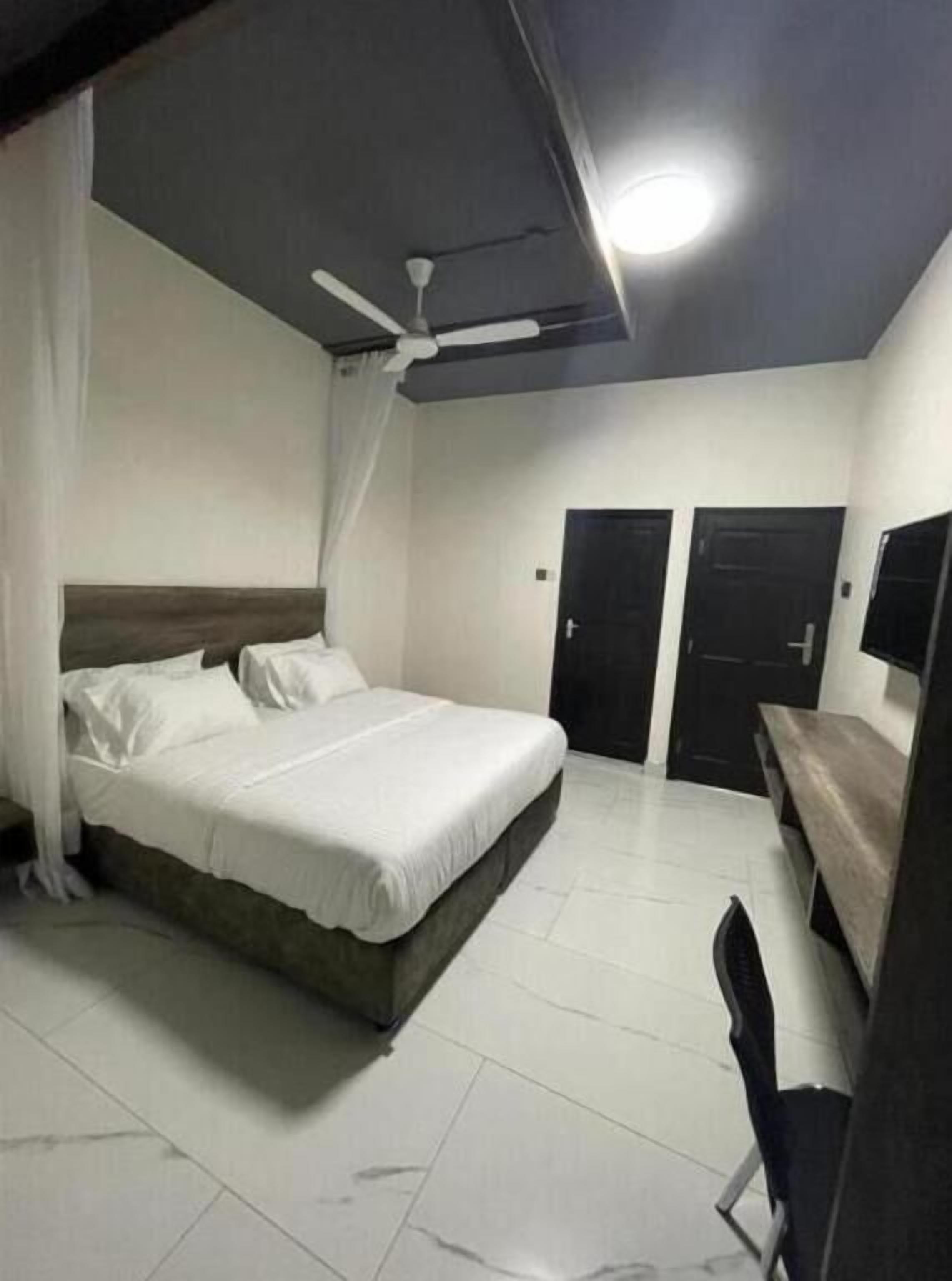 A bedroom with a bed, a ceiling fan, a desk, and two doors.