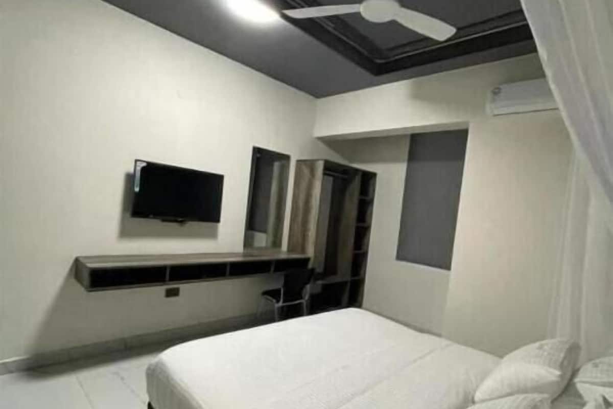 Un dormitorio moderno con una cama, ventilador de techo, televisor montado y estante empotrado.