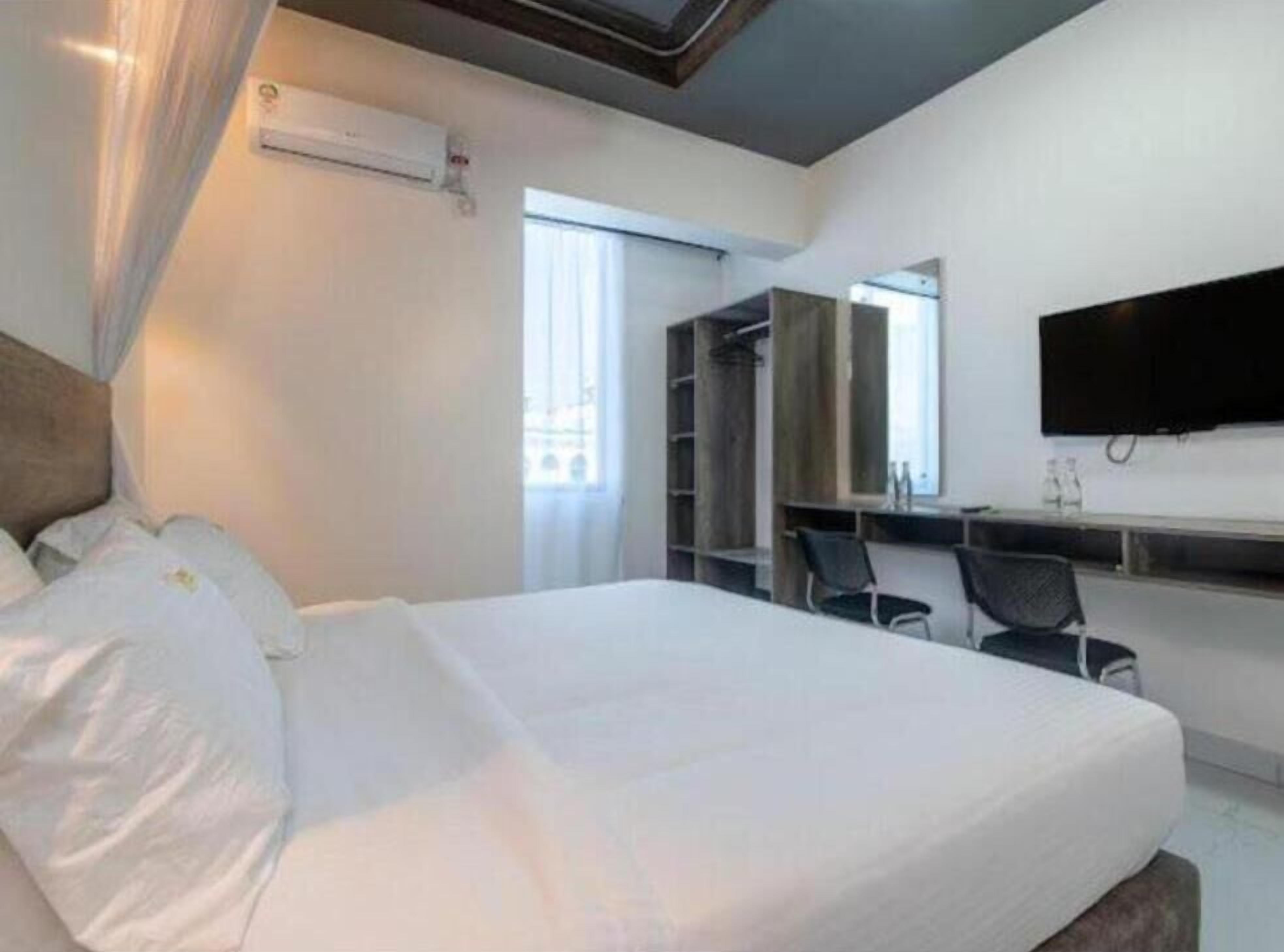Una habitación de hotel con una cama, un escritorio, una silla, un televisor y un armario.
