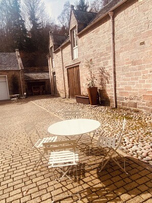 A courtyard with a round table and chairs, a potted plant, and a stone wall. - Brylach Steading (Aberlour)