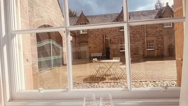 Une fenêtre donnant sur une cour, un bâtiment en briques et une table avec deux bouteilles.