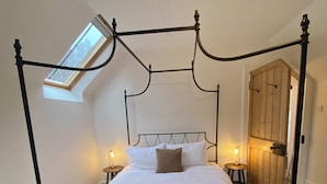 Un lit à baldaquin avec une couvre-lit à carreaux, une lucarne au-dessus, des lampes de chevet et une armoire en bois.