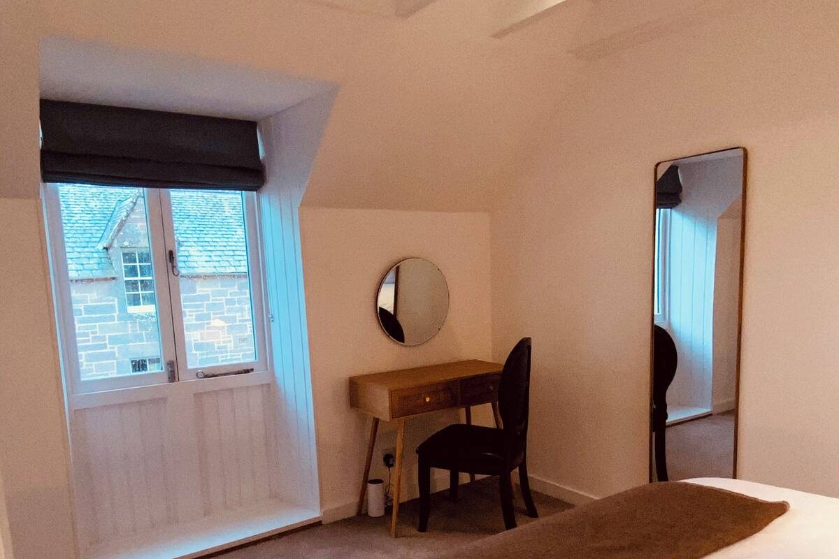 Un dormitorio con cama, escritorio, silla, ventana y espejo.