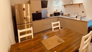Une cuisine moderne dotée d’appareils électroménagers en acier inoxydable, d’une table à manger en bois et de luminaires suspendus.