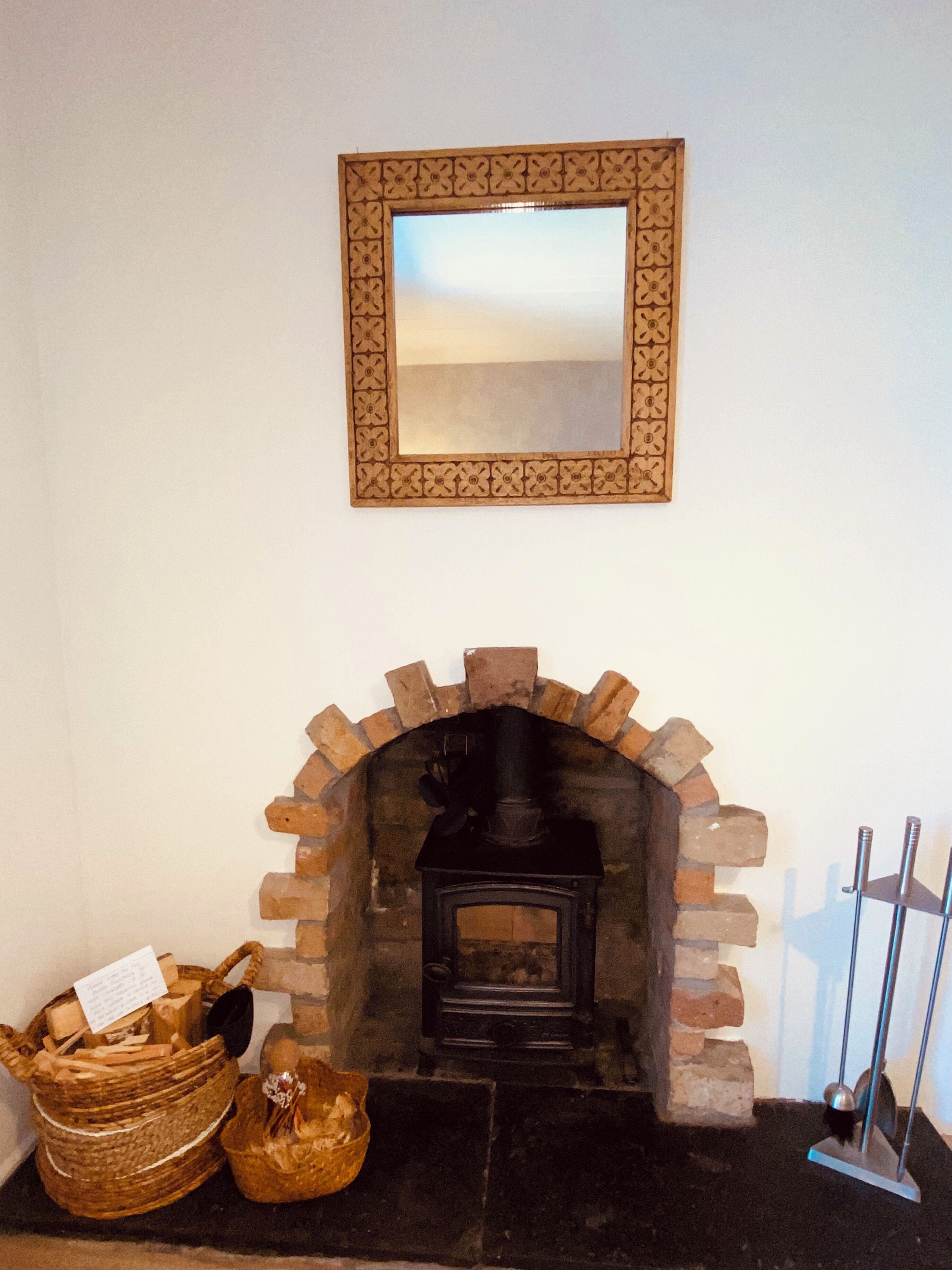 Une cheminée avec une arche en briques, un miroir au-dessus et un support en métal sur la droite.