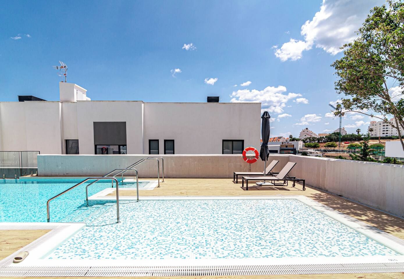 Une piscine sur le toit offrant une vue dégagée sur le paysage urbain, une bouée de sauvetage et des chaises longues.