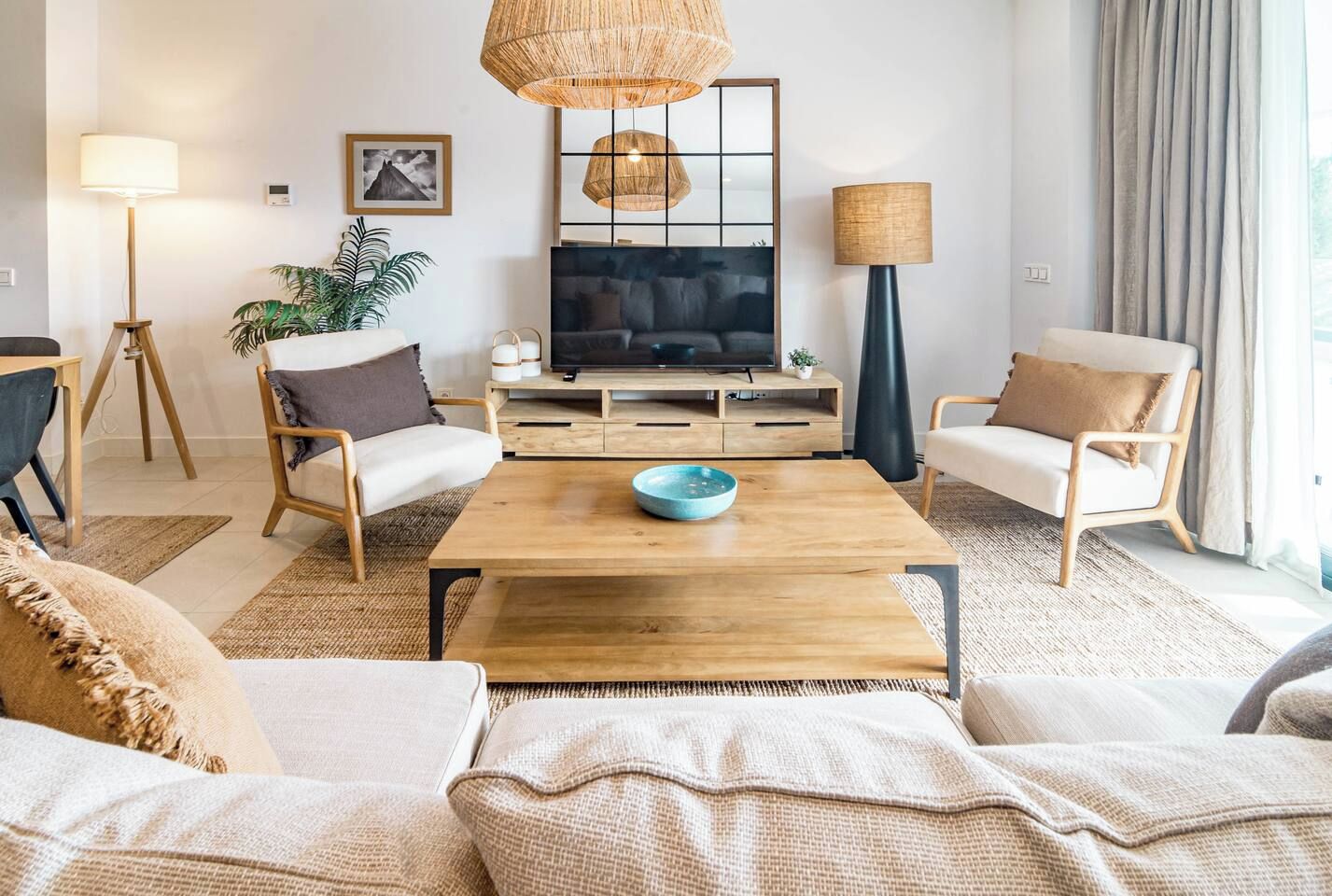 Un salon moderne avec une table basse en bois, deux canapés, un téléviseur et une grande fenêtre avec des rideaux.