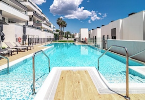 A swimming pool with a wooden deck, metal railings, and a clear blue sky. - Lme3bb - Modern Flat With a Stunning 50 m² Terrace (Estepona)