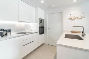 A modern kitchen with white cabinetry, a built-in oven, a microwave, a sink with a contemporary faucet, and decorative scales on the wall. - Lme3bb - Modern Flat With a Stunning 50 m² Terrace (Estepona)