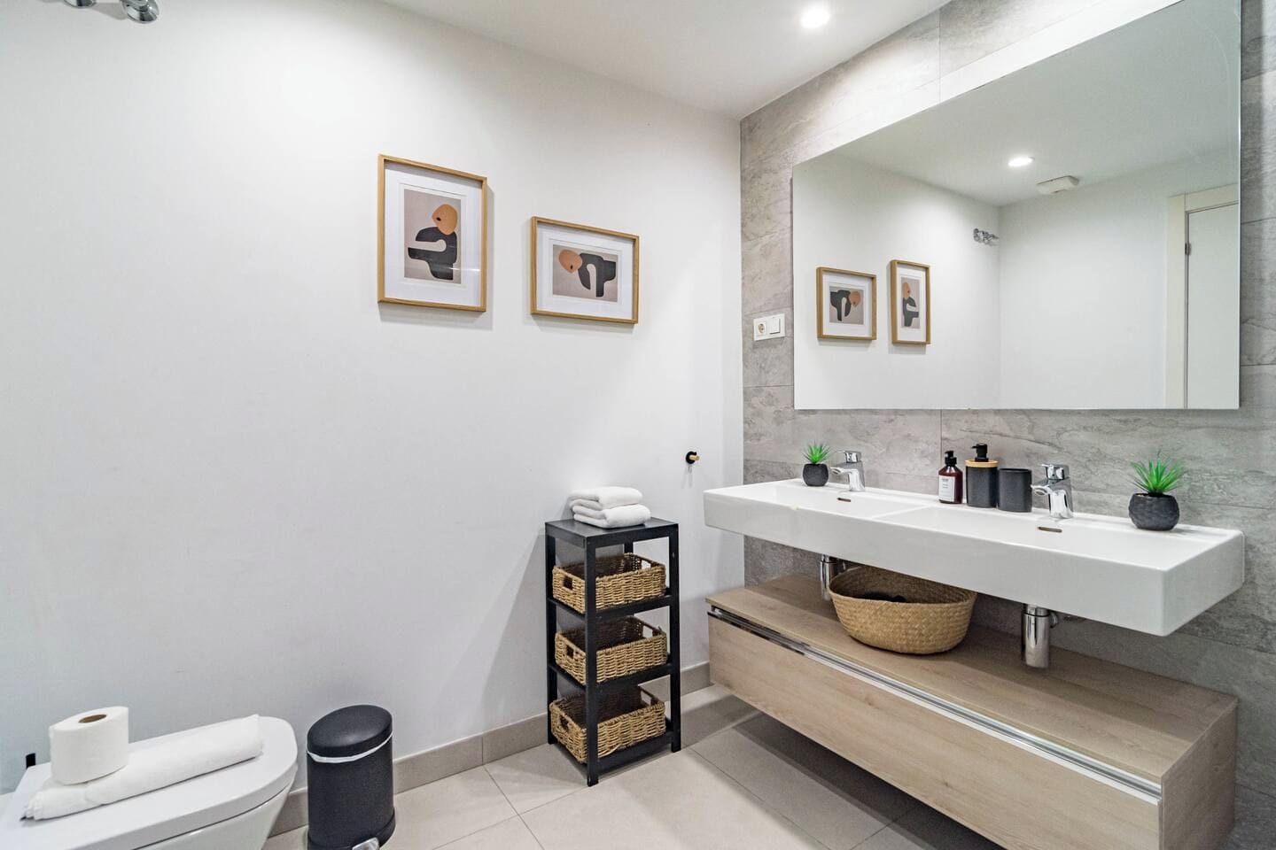 Une salle de bain moderne avec un lavabo blanc, un grand miroir et des œuvres d’art encadrées accrochées au mur.