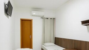 A hotel room with three single beds, a TV mounted on the wall, an air conditioning unit, and a wooden door. - Nova Jerusalém Hotel (Goiânia)