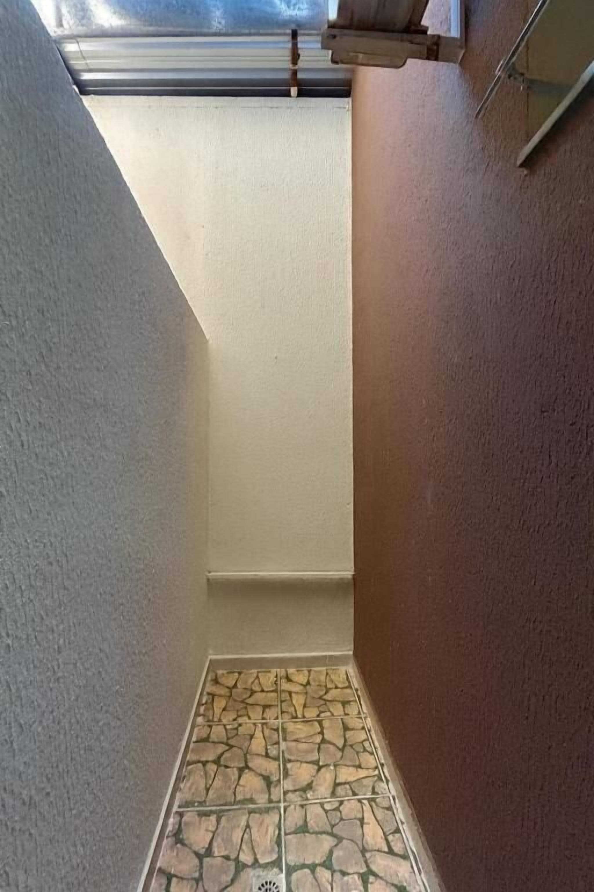 A narrow hallway with a sloped ceiling and stone-patterned floor tiles.