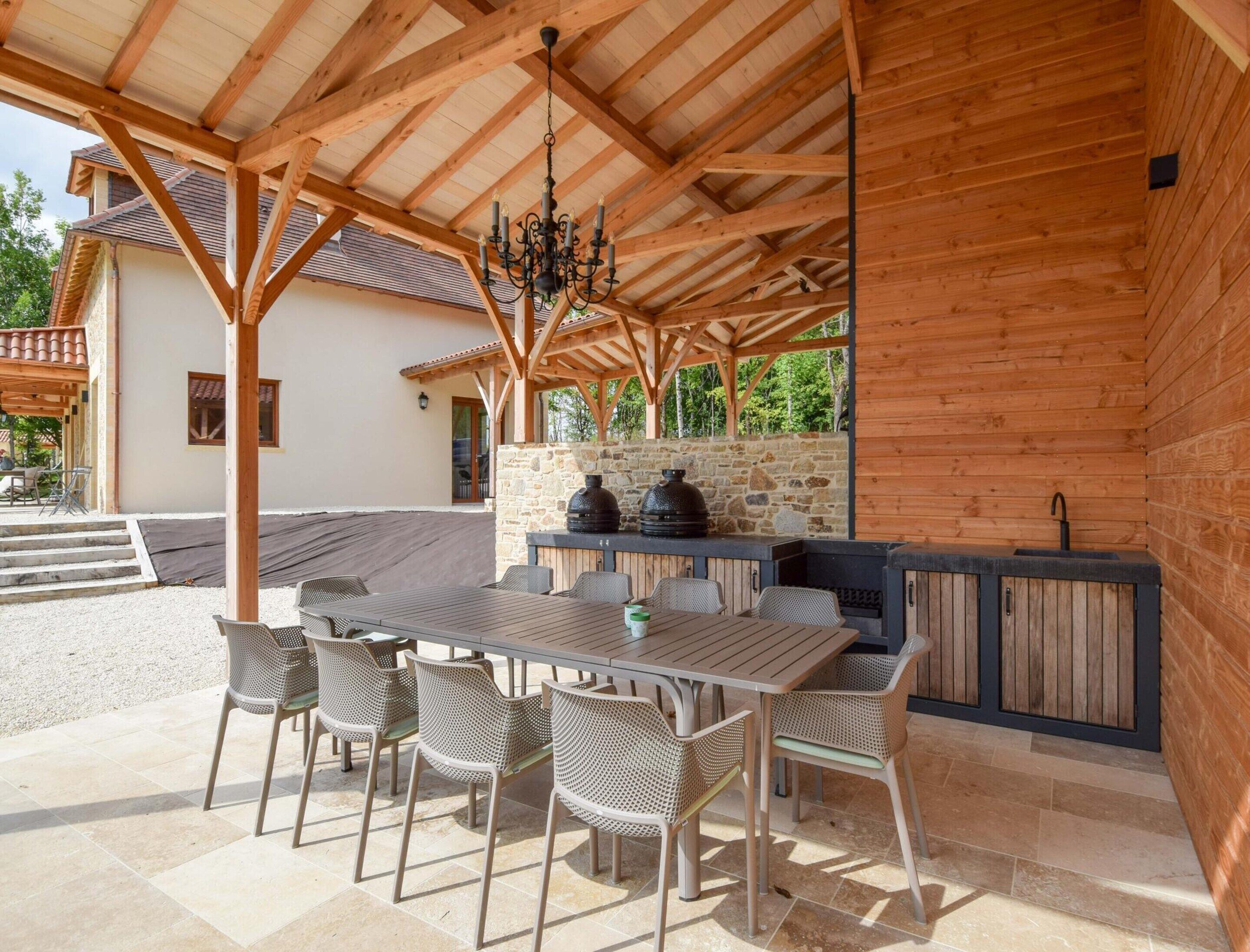 An outdoor patio with a wooden pergola, stone wall, and a built-in grill station.