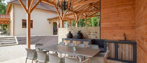 An outdoor patio with a wooden pergola, stone wall, and a built-in grill station.