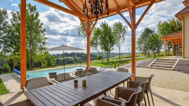 Ein überdachter Außenbereich mit Pool, Esstisch und Stühlen mit Blick auf eine malerische Landschaft.