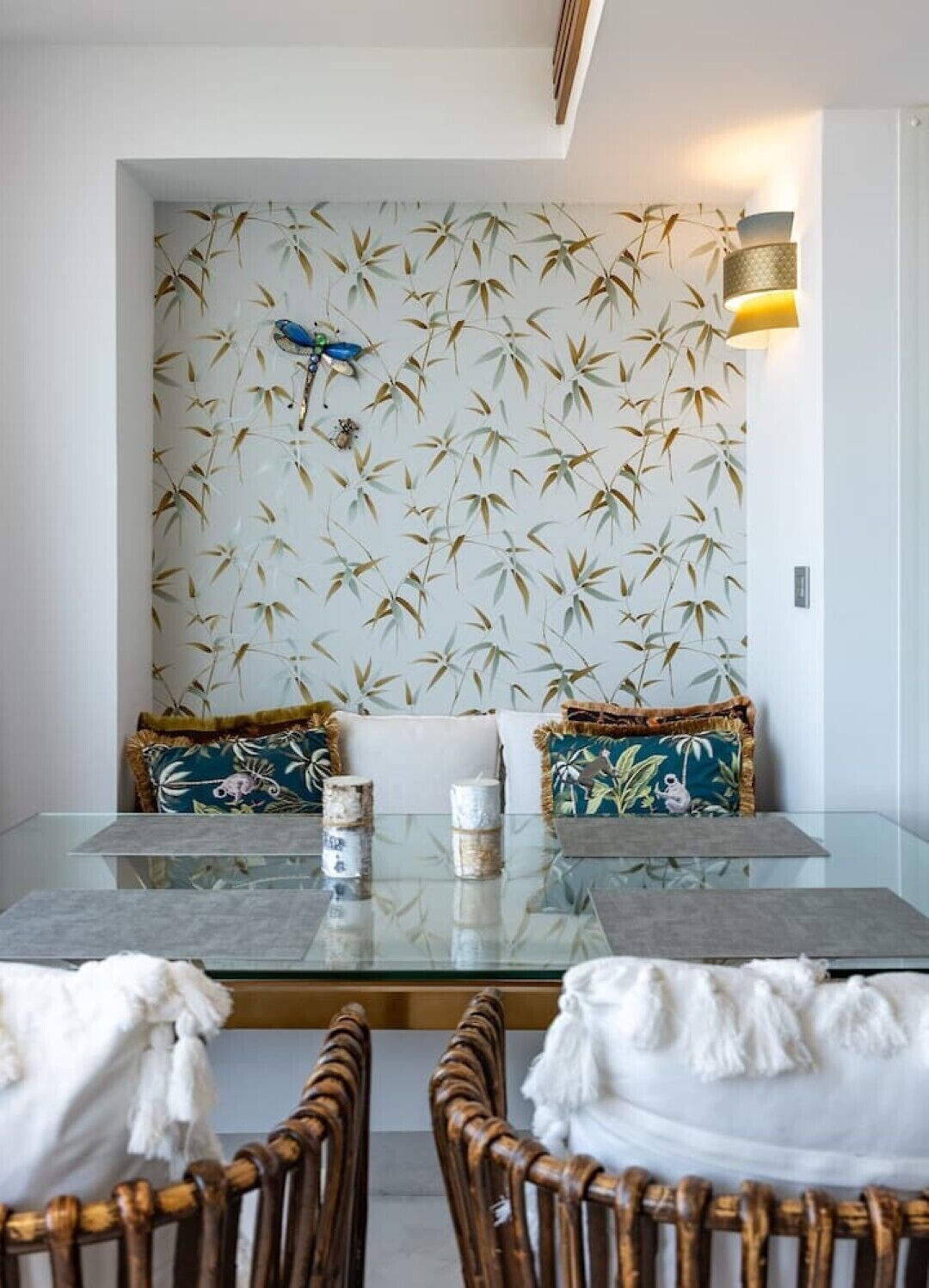 Un comedor con una mesa de vidrio, dos sillas y una pared con diseño de hojas de bambú.