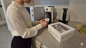 En person i et køkken laver en drik med en kaffemaskine og en kasse med teksten 'today 1 increase T.F.A'.