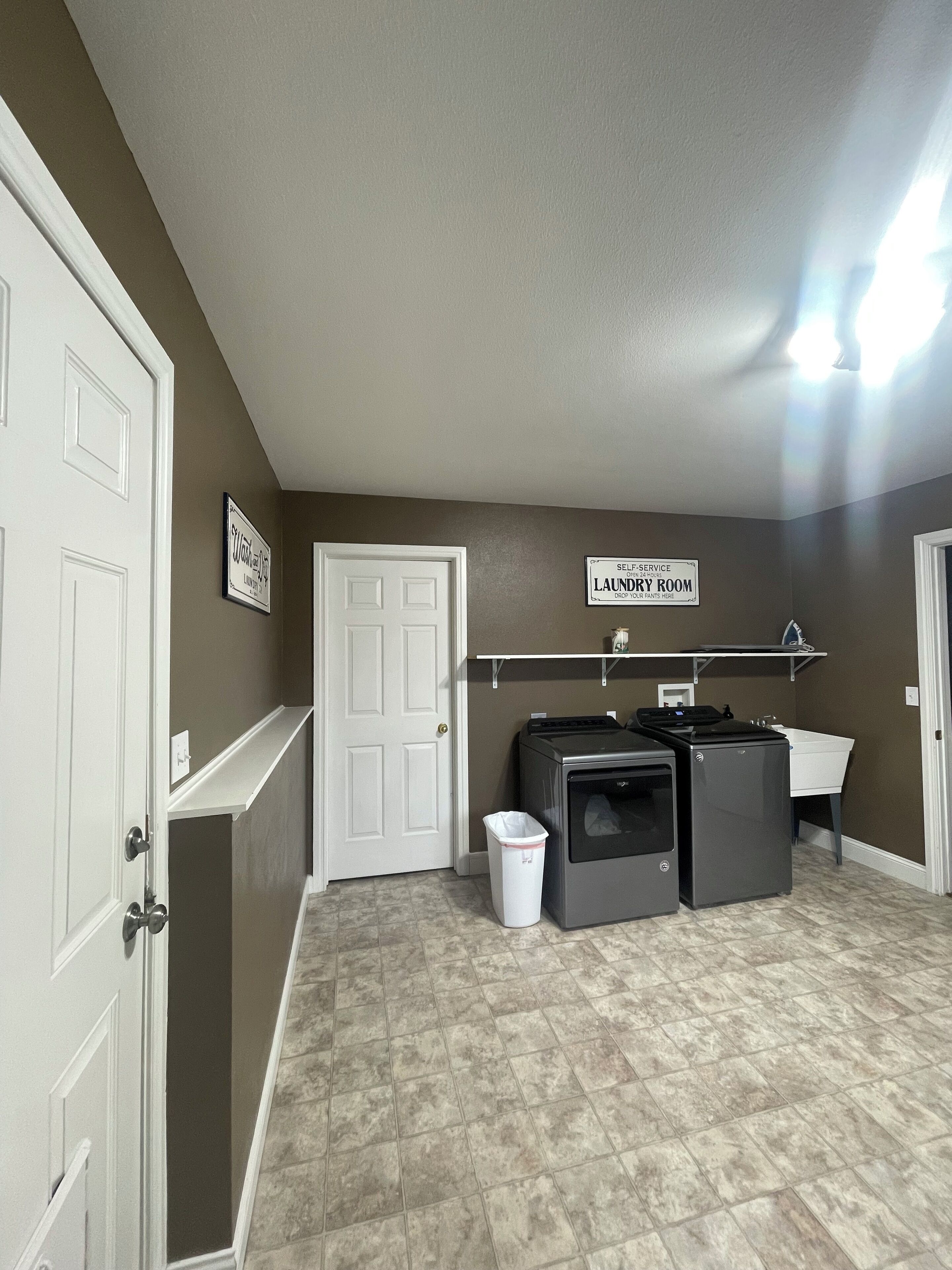 A laundry room with a washing machine, a sink, and a trash bin.