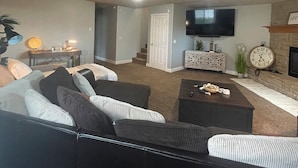 A living room with a sofa, coffee table, and a fireplace. There is a television mounted on the wall and a clock on the mantel. - Spacious 5-bedroom house in a quiet part of Billings close to entertainment. (Billings)