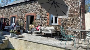 A stone building with a sign reading 'The Dairy,' outdoor seating with a table and chairs, and a large umbrella providing shade. - The Dairy (Holsworthy)