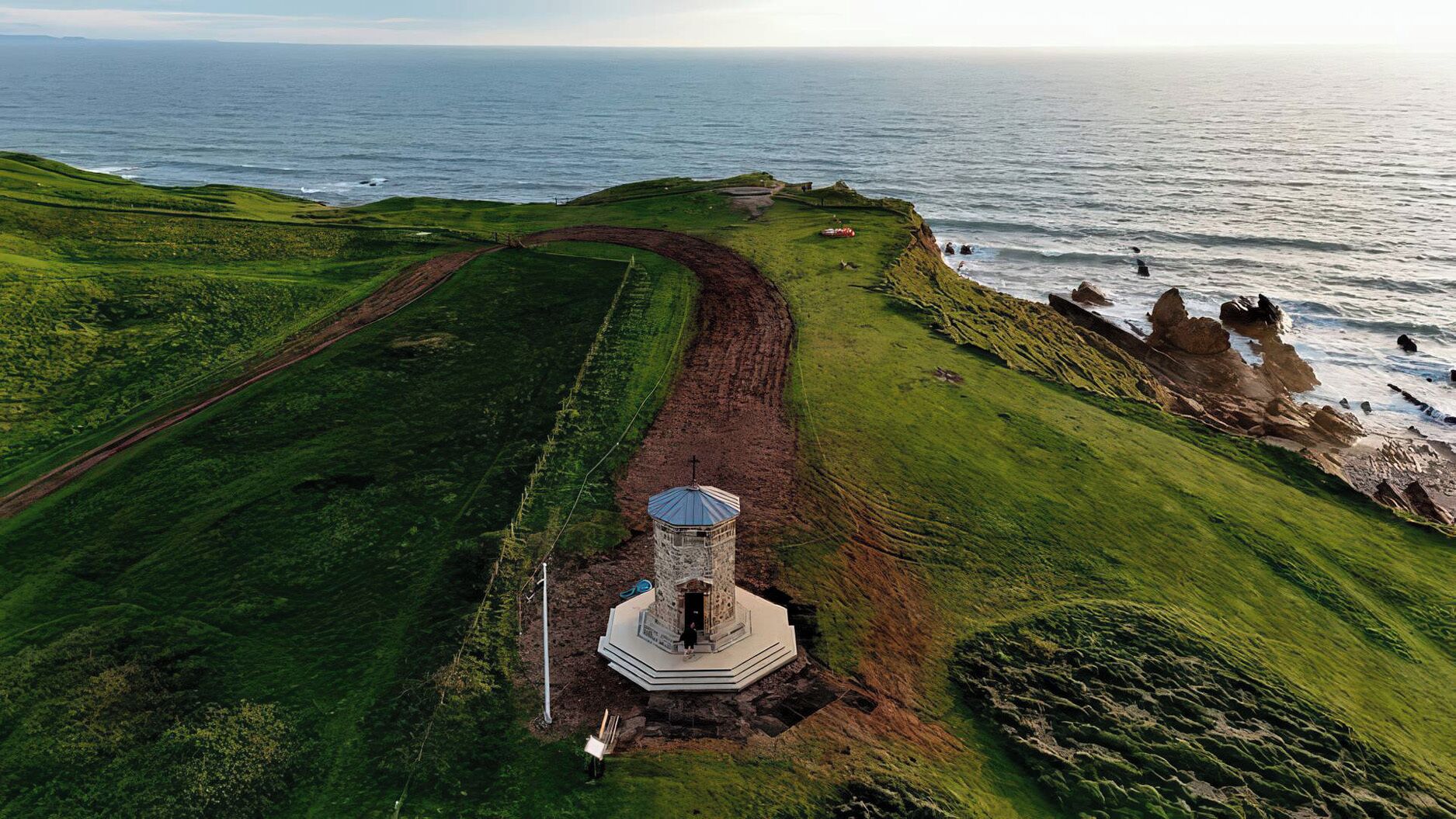 Un paysage côtier avec un phare, des champs verdoyants et une vue dégagée sur la mer.