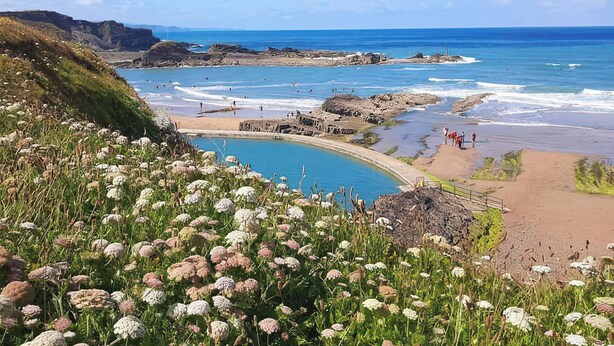 A coastal landscape with a clear blue sky, a beach, and a pool area. - The Dairy (Holsworthy)