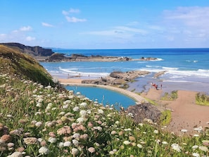 Paesaggio costiero con cielo azzurro limpido, spiaggia e area piscina.