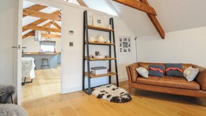 A loft-style room with a wooden ceiling, a brown leather sofa, a white rattan bench, and a dog bed. - The Dairy (Holsworthy)