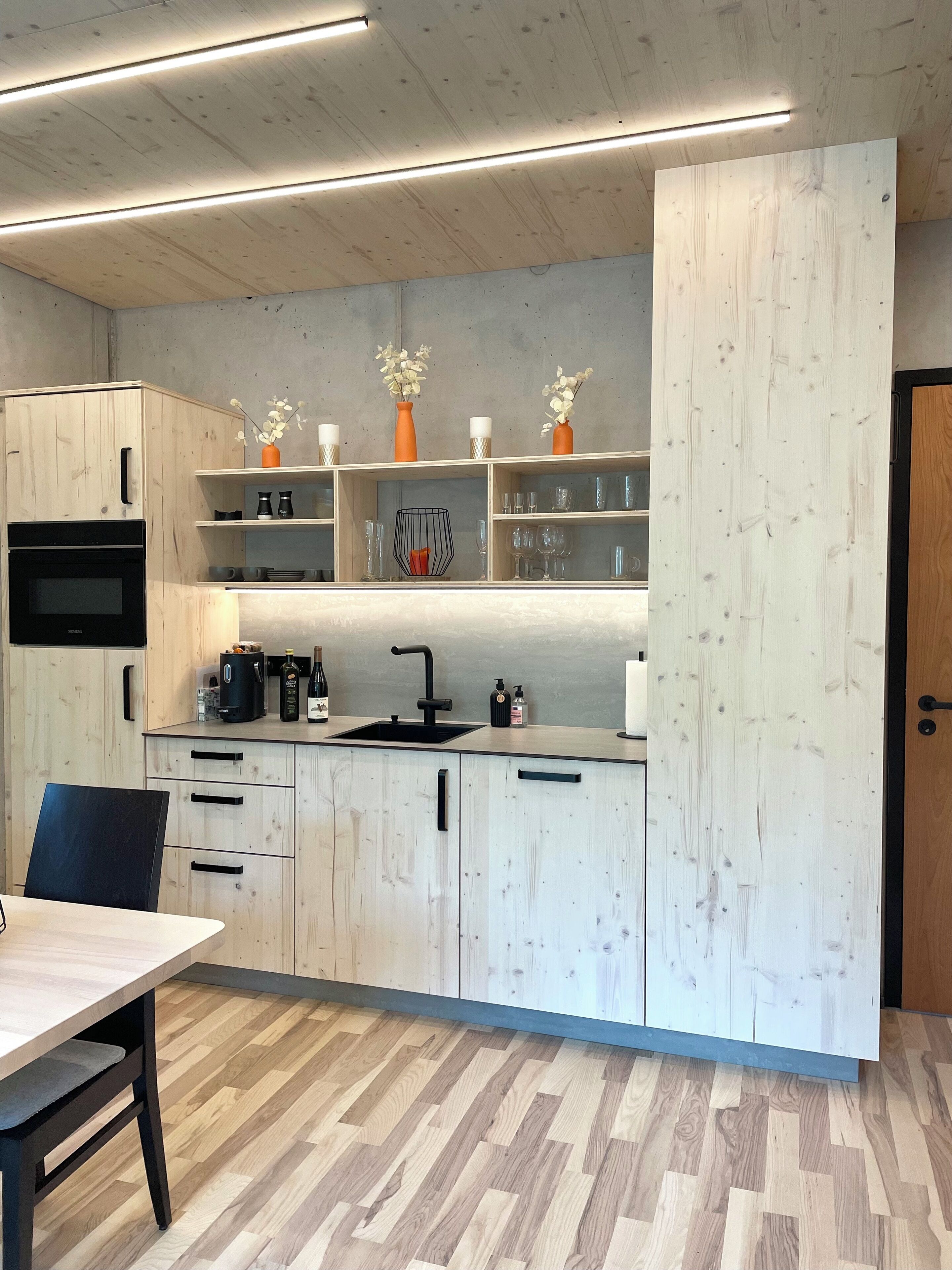 Une cuisine moderne avec des meubles en bois, un plan de travail noir et un four encastré. On y trouve également un coin repas avec une table et des chaises.