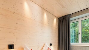 Ein Schlafzimmer mit zwei Betten, Holzwänden, einem Fenster mit Vorhängen und einem Nachttisch mit einem Buch.