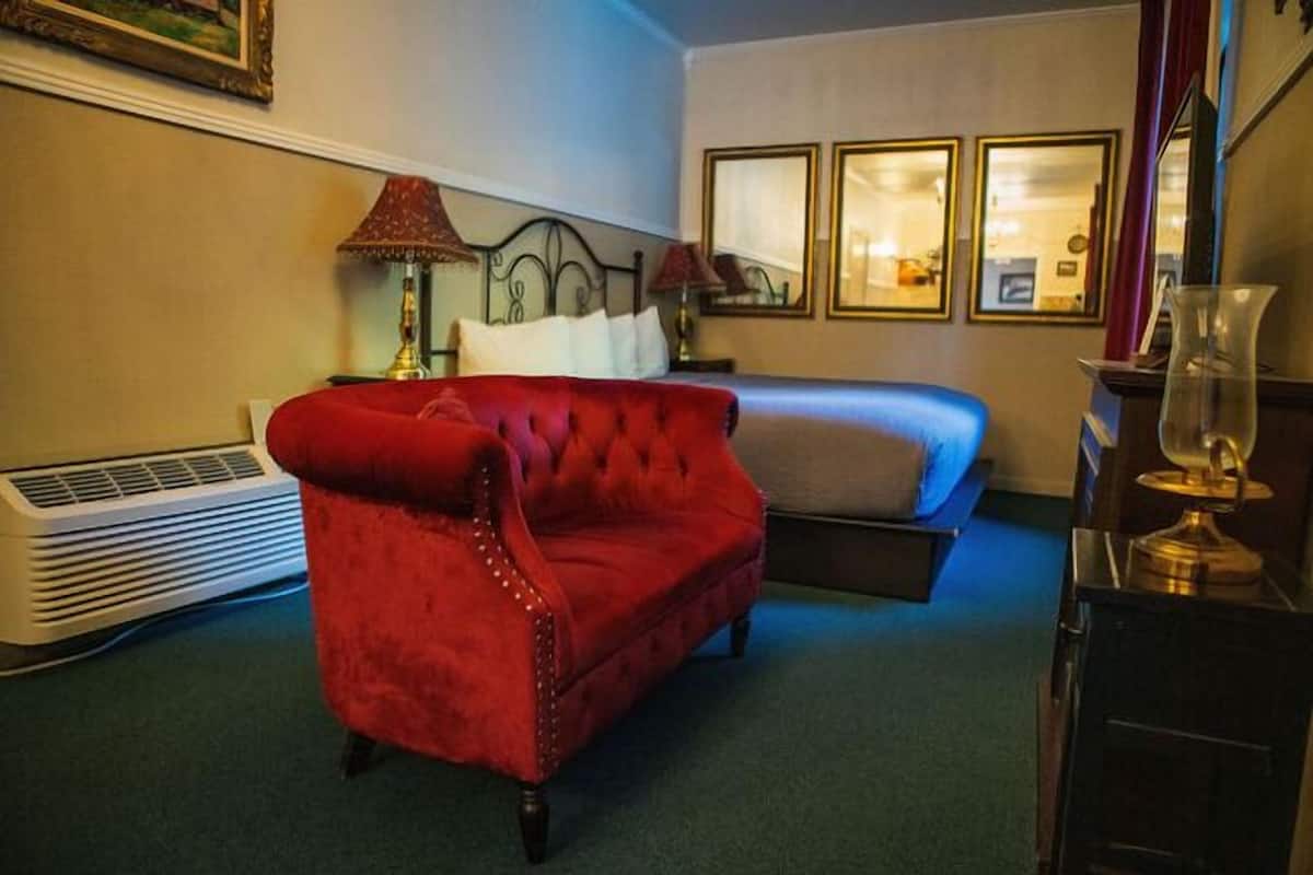 Ein Hotelzimmer mit einem roten Stoffstuhl, einem Bett, einem Nachttisch mit Lampen und einer Heizung.